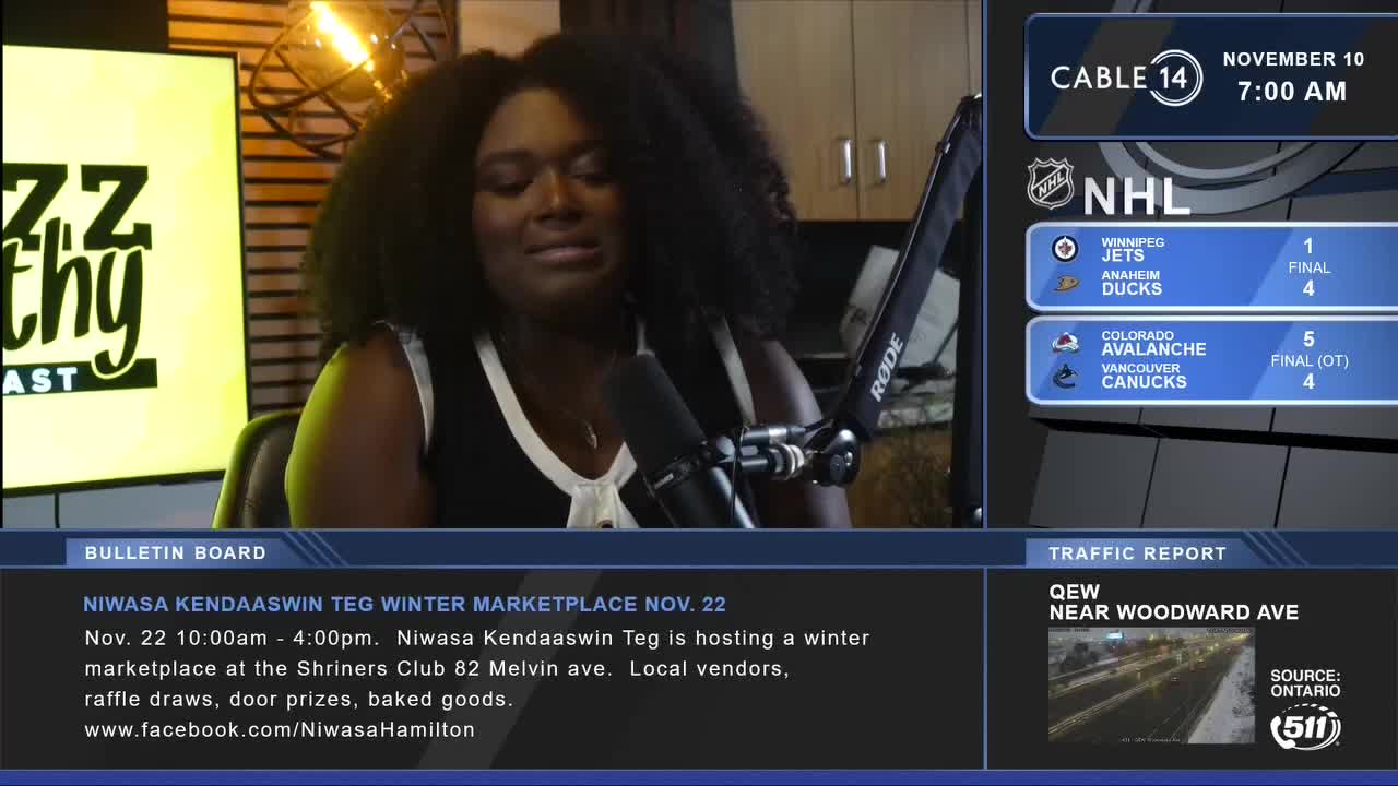 A woman with dark curly hair sits in front of a microphone, speaking on Cable 14 Hamilton. The screen displays hockey scores and a bulletin about a winter marketplace in Canada.
A woman with dark curly hair sits in front of a microphone, speaking on Cable 14 Hamilton. The screen displays hockey scores and a bulletin about a winter marketplace in Canada.