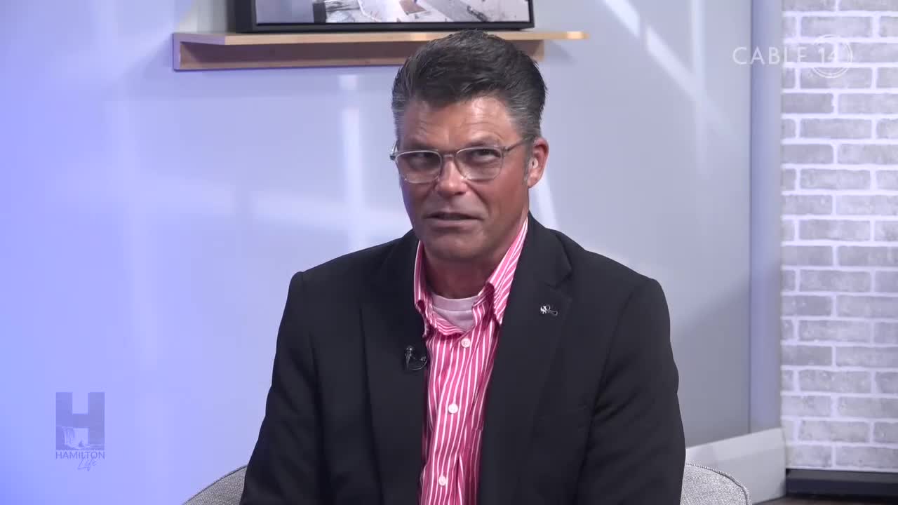 A man in a suit jacket and glasses is speaking on a Cable 14 Hamilton set. The background is a soft blue with the station's logo in the corner.
A man in a suit jacket and glasses is speaking on a Cable 14 Hamilton set. The background is a soft blue with the station's logo in the corner.