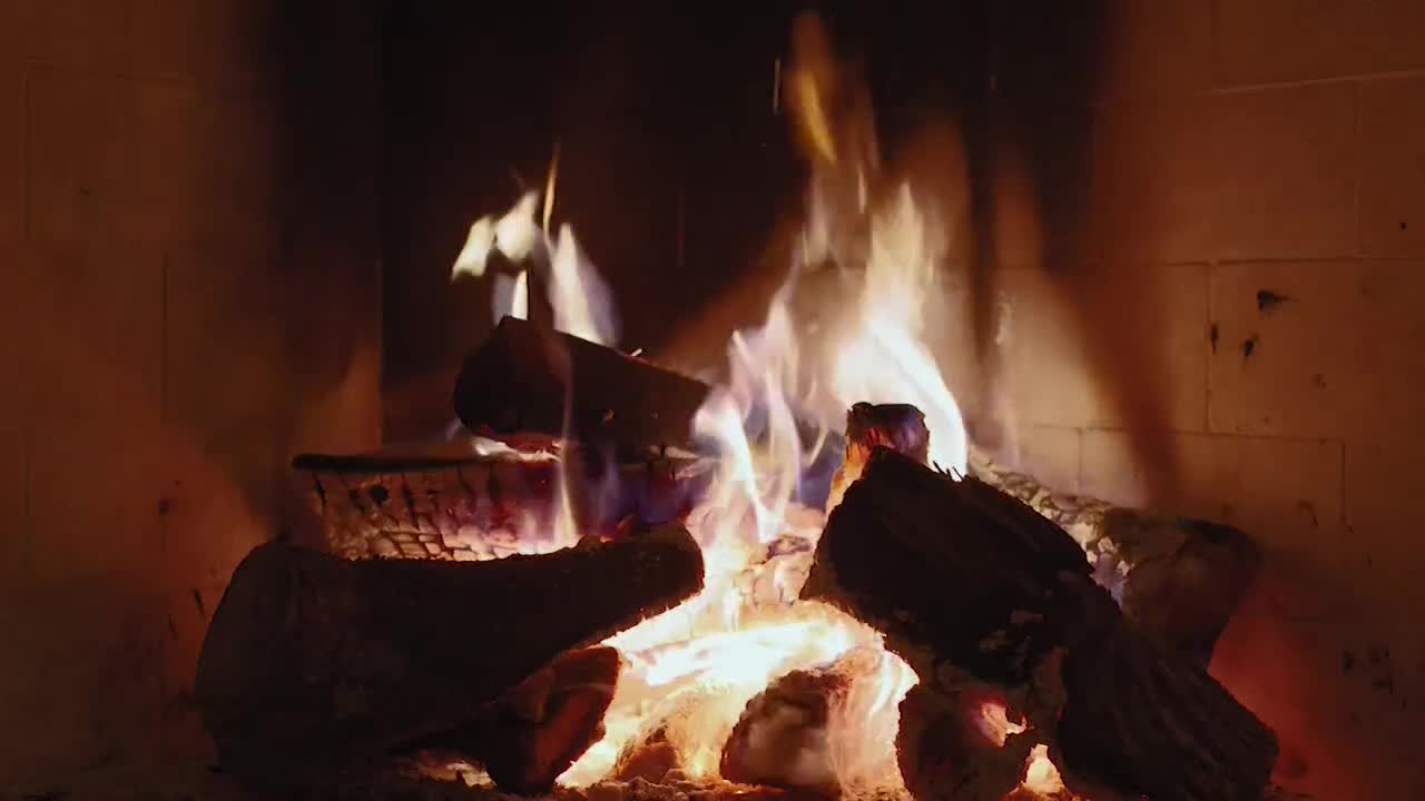 Flames lick at the logs, their orange and yellow light dancing against the dark brick. The wood crackles and pops, sending sparks into the air.
