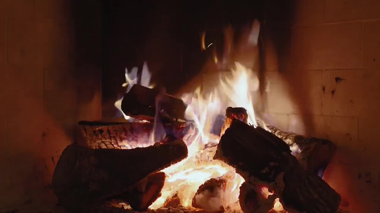 Flames dance above the burning logs, their orange and yellow hues contrasting with the dark brick of the fireplace. The fire crackles gently, a warm glow filling the room.
