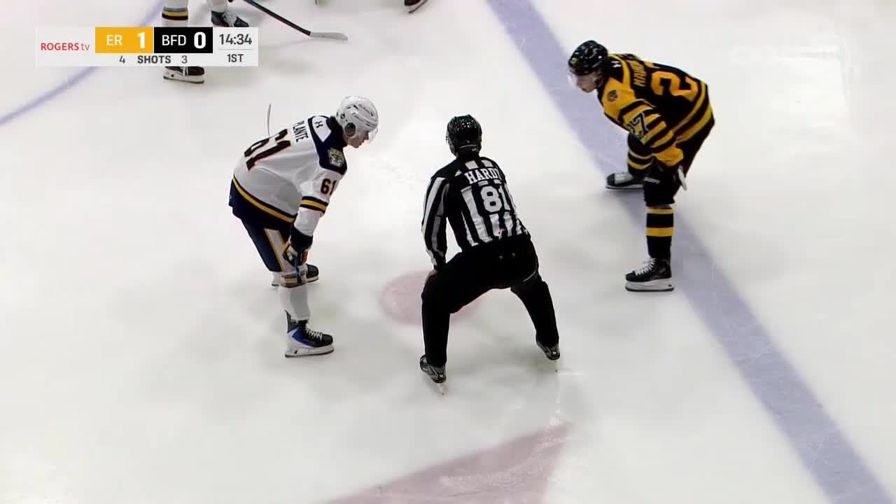 The referee stands between two players, ready to drop the puck for the faceoff. The scoreboard shows the score is 1-0, with the game in the first period.