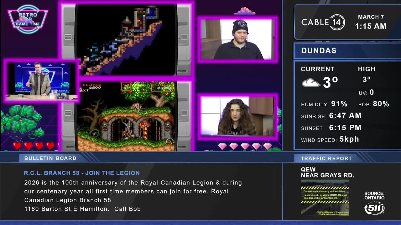 A man in a suit stands at a desk, gesturing towards a screen displaying a retro video game. On Cable 14 Hamilton, the weather report for Dundas shows a current temperature of 3 degrees Celsius.