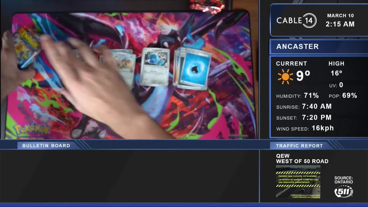 A hand slides a Pokémon card pack across a vibrant mat. Several cards, including one with a blue water symbol, are already laid out.