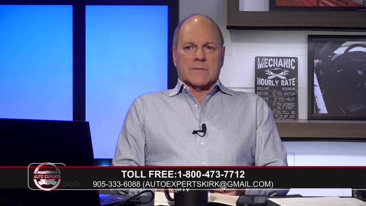 A man in a light blue collared shirt sits at a desk, looking directly ahead. A graphic at the bottom of the screen displays "AUTO EXPERTS" and contact information.