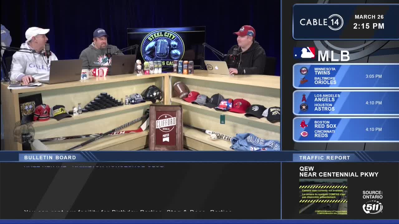 Three men are seated behind a counter, discussing baseball on Cable 14 Hamilton. A screen displays upcoming MLB games and traffic information for the QEW.