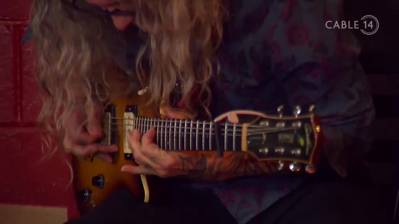 Fingers fly across the fretboard of a sunburst electric guitar, the strings vibrating with each strum. The Cable 14 Hamilton logo is visible in the corner, a reminder of this Hamilton performance.