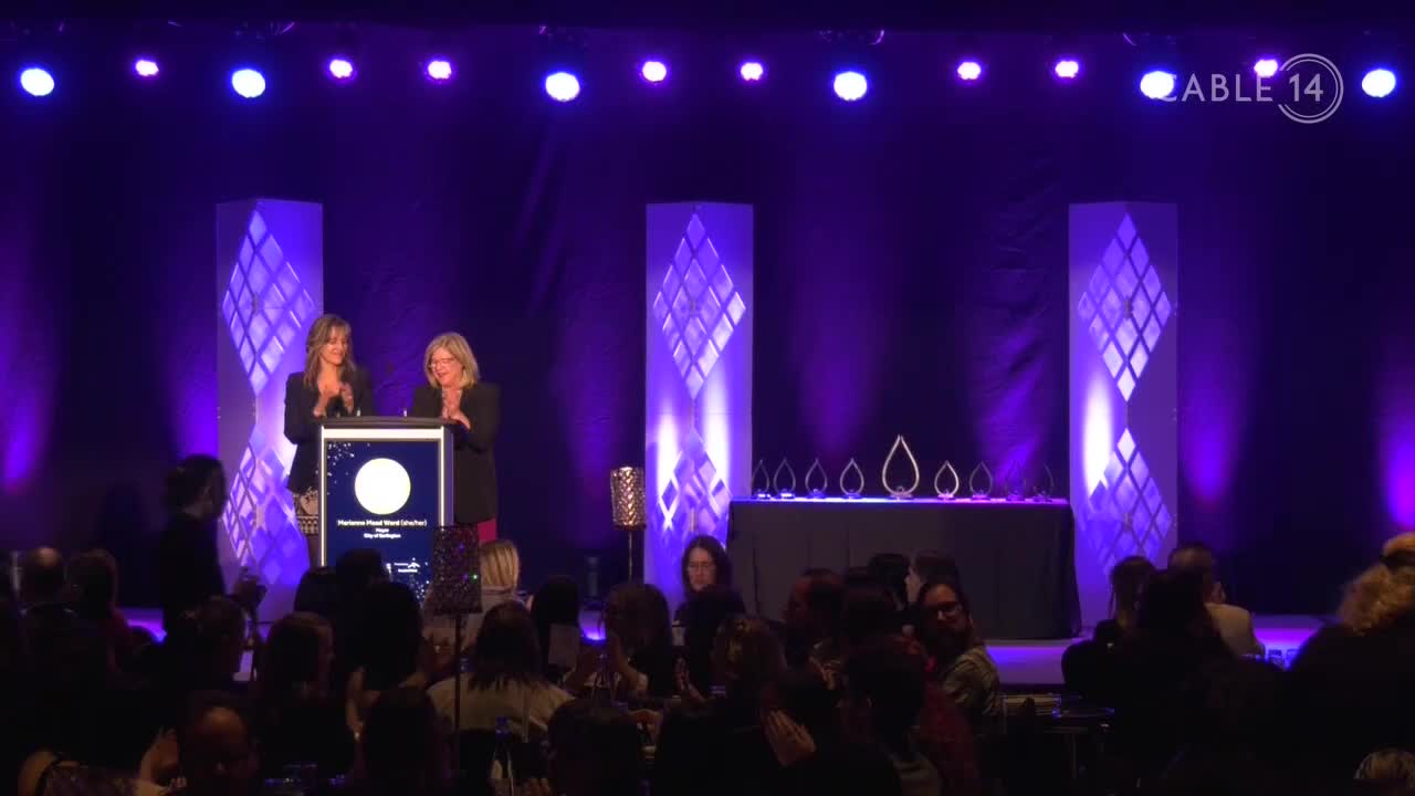 Two women stand at a podium, acknowledging applause from the audience. The stage is lit with purple spotlights, and a Cable 14 Hamilton logo is visible in the upper right corner.