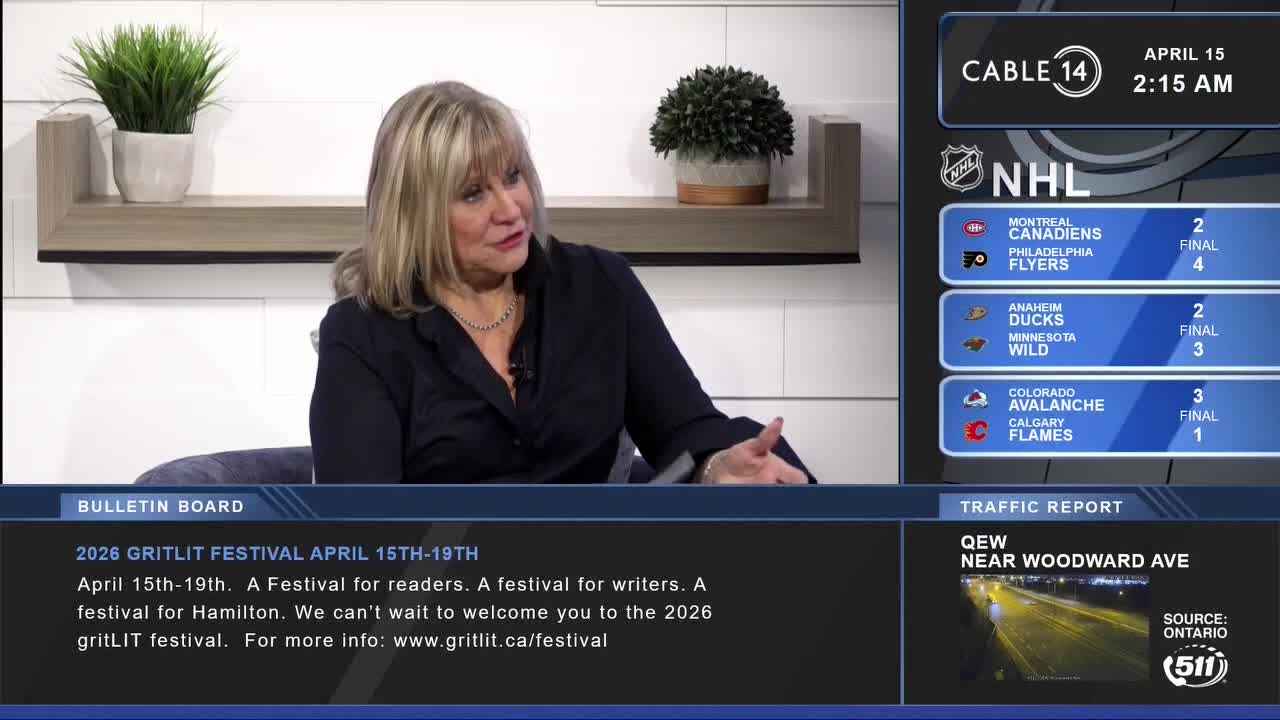A woman with blonde hair is speaking into a microphone, gesturing with her hands. On the screen behind her, Cable 14 Hamilton displays NHL scores and traffic information for the QEW near Woodward Ave.