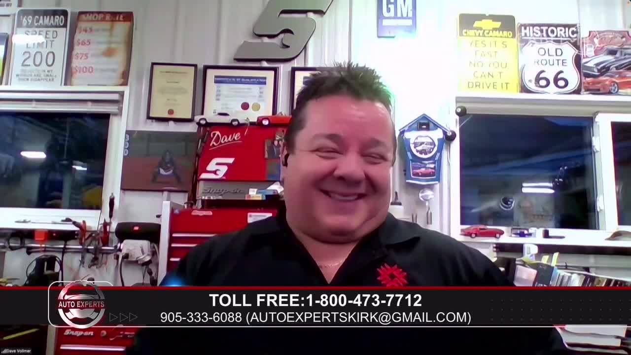 A man with dark hair and a wide smile is speaking, likely for Cable 14 Hamilton. He's in a workshop, with tools and car-themed memorabilia visible behind him.