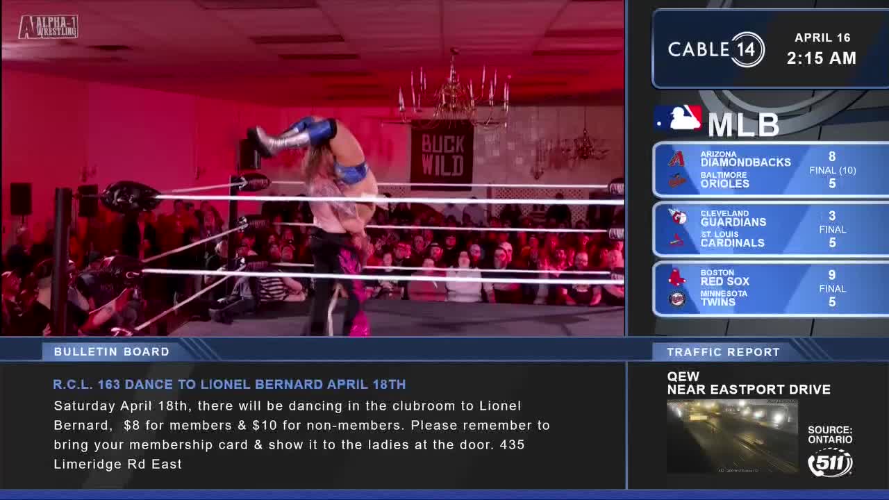 One wrestler lifts another in a suplex hold over the wrestling ring. The crowd watches intently from the sidelines as the action unfolds.