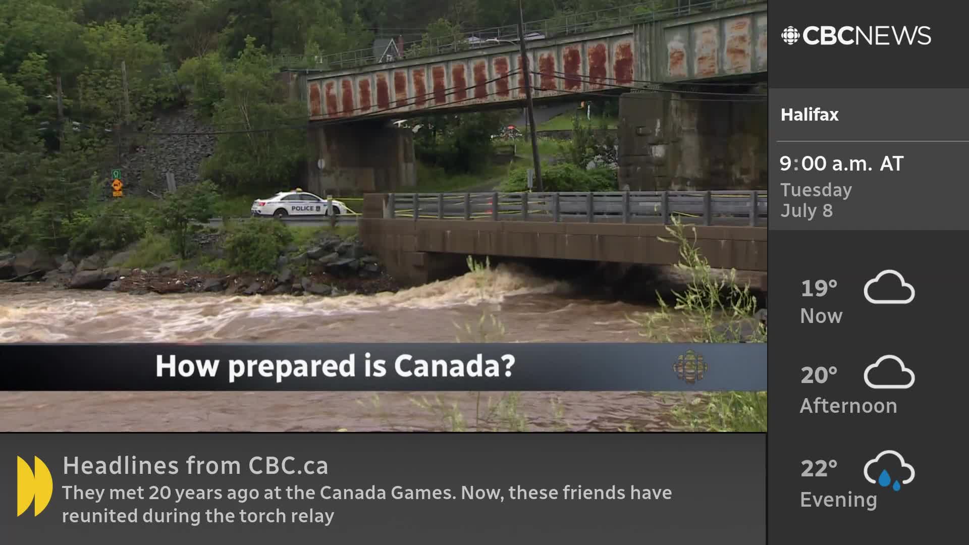 The swollen river rushes under a bridge, its murky water churning. A police car is parked on the road above, and the CBC News Network is asking about Canada's preparedness.
