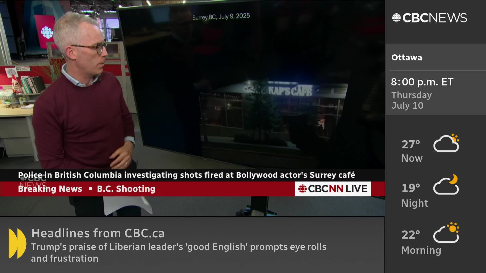 A man in a maroon sweater stands beside a large screen showing a cafe in Surrey, British Columbia. The CBC News Network logo is visible, with a breaking news banner below.
