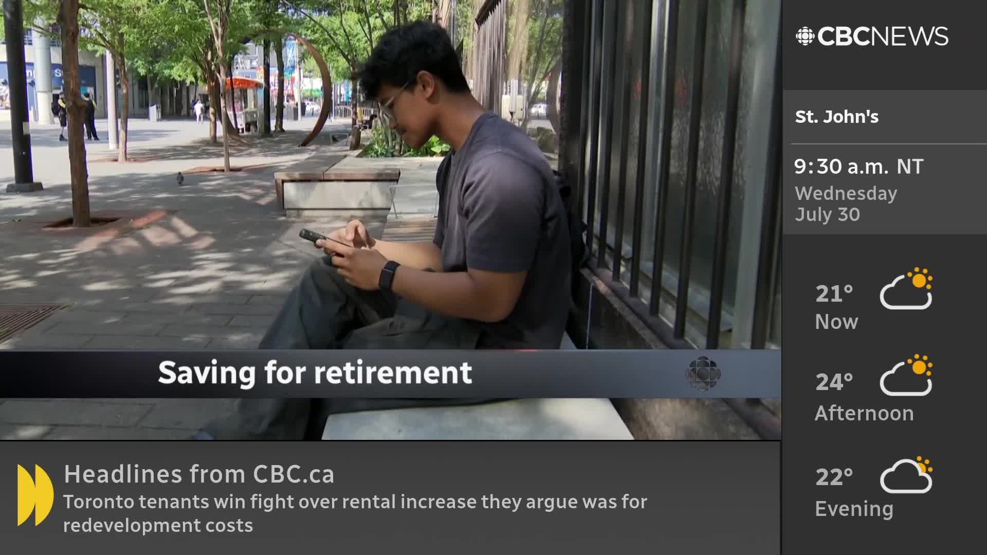 A man in glasses sits on a bench, intently looking at his phone. The CBC News Network graphic indicates it's a warm morning in St. John's, Newfoundland.
