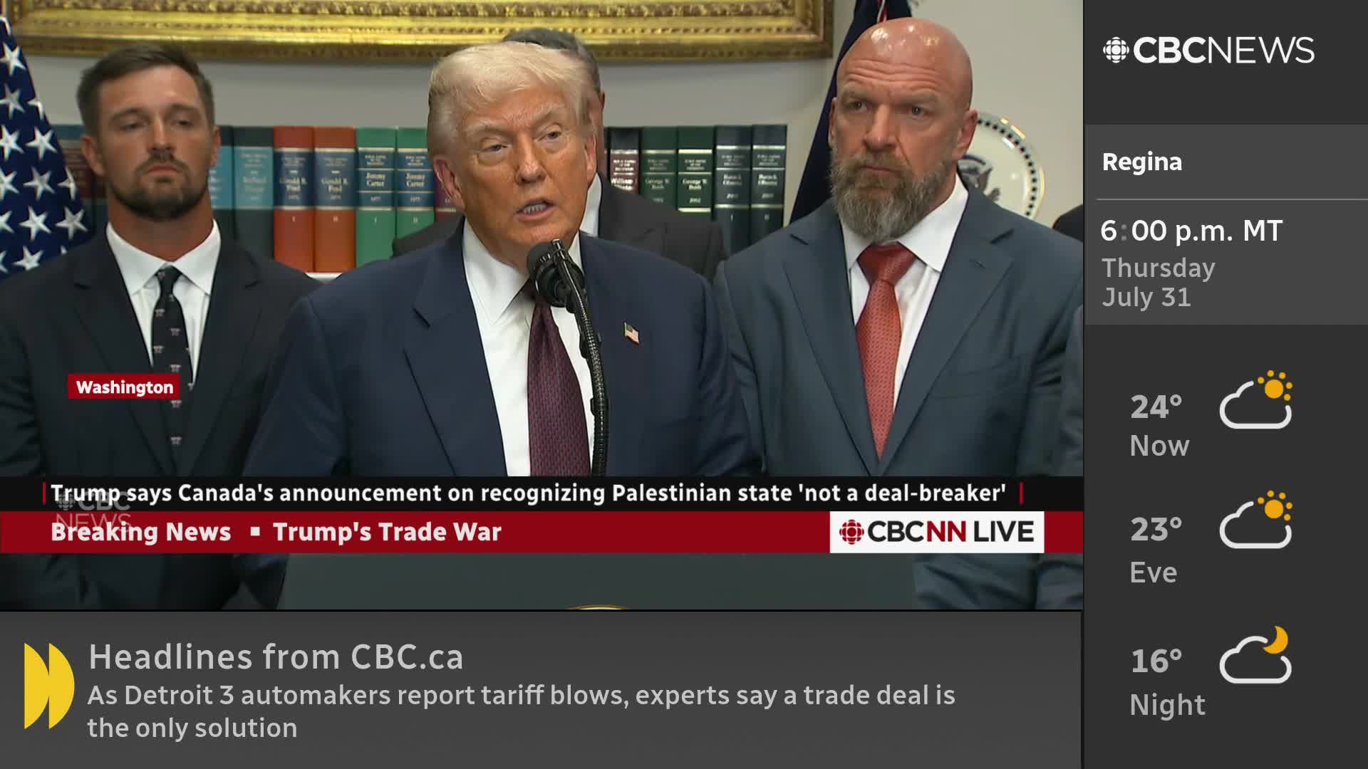 A man in a suit speaks into a microphone, flanked by two others, as a CBC News Network graphic displays below. The headline on the screen references Canada and a trade war.
