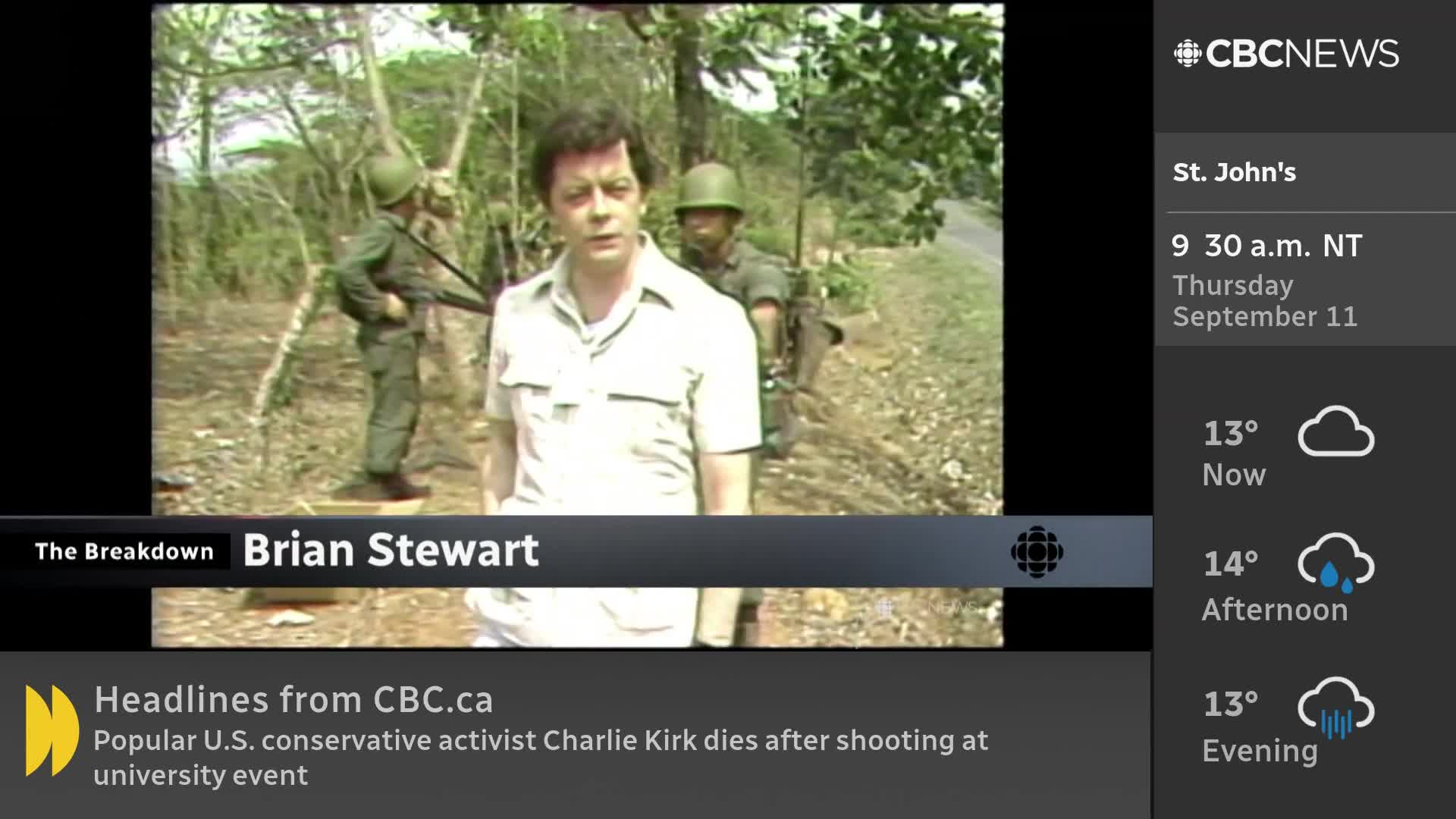 A CBC News reporter, Brian Stewart, stands in front of two soldiers, speaking directly to the camera. The scene is set outdoors, with trees and a road visible in the background.

