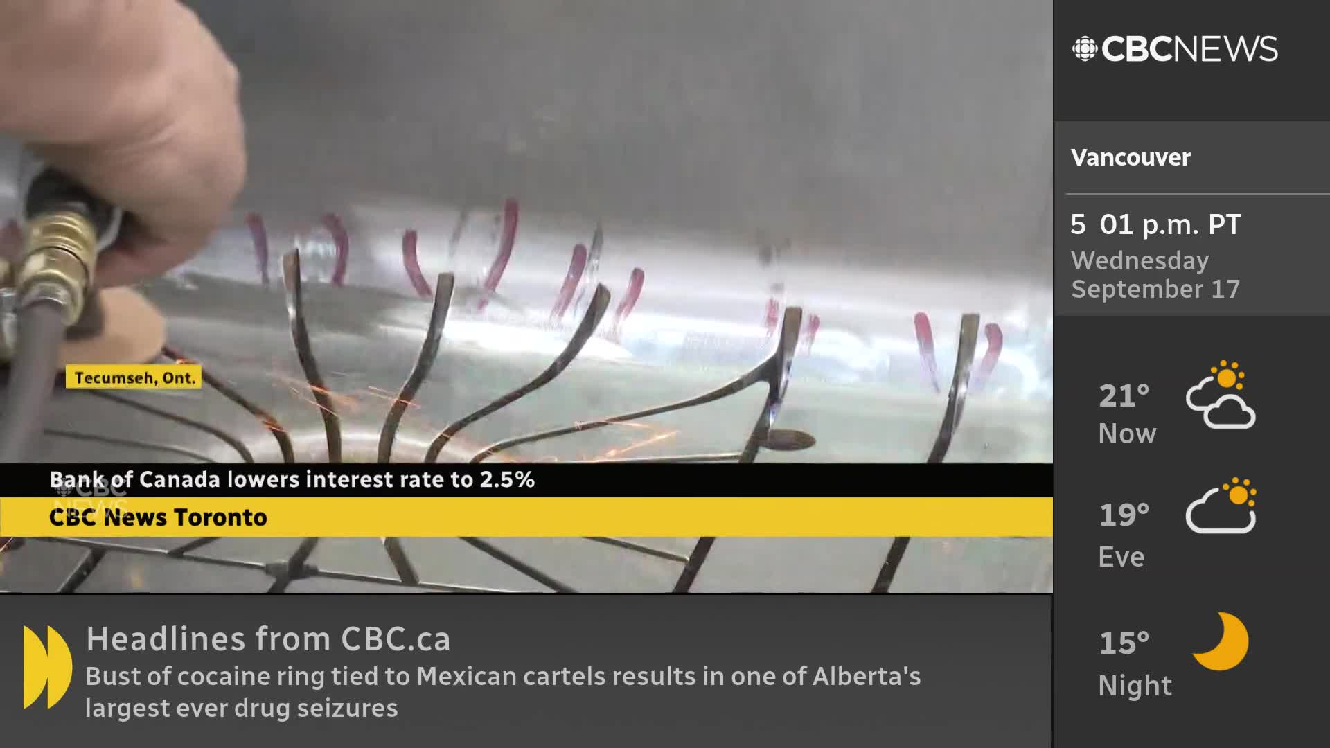 A hand holds a tool, sending sparks across the metal surface. The CBC News Network broadcast shows the scene, with a headline about the Bank of Canada.
