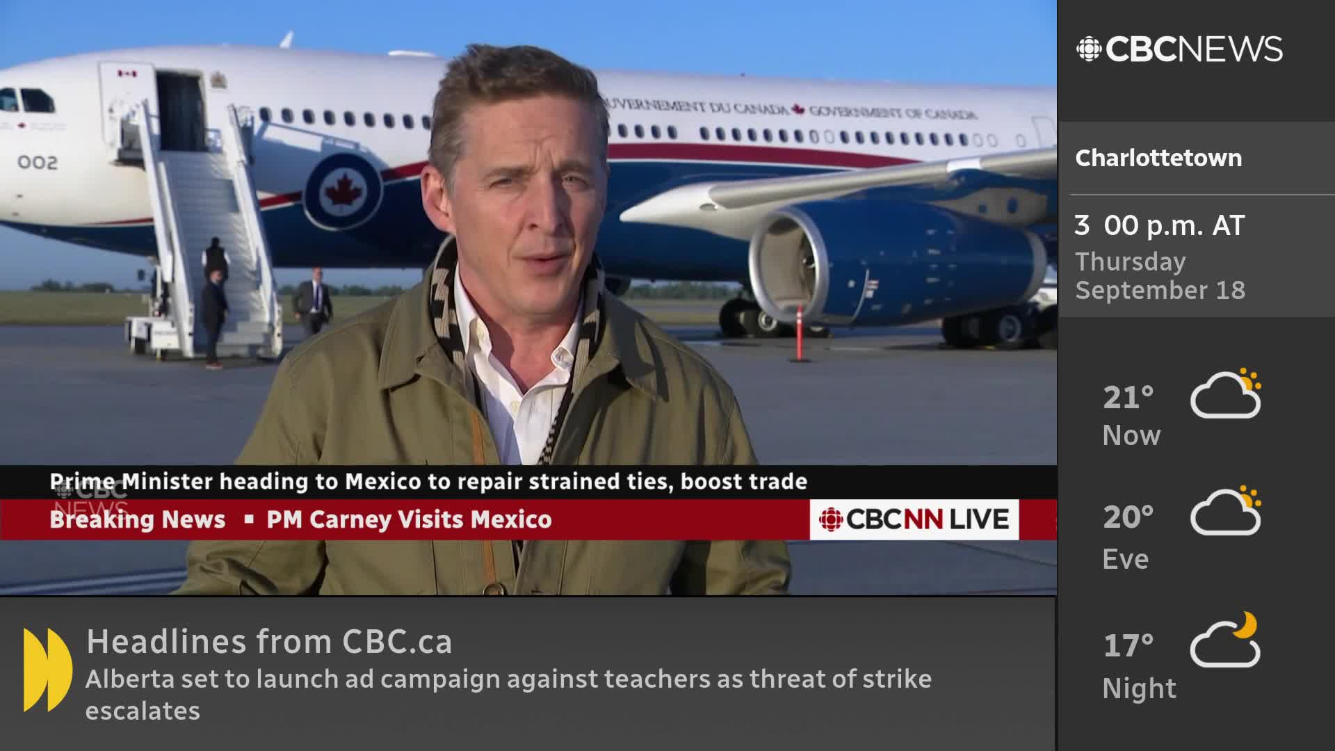 A CBC News Network reporter stands in front of a Canadian government plane, speaking on camera. Behind him, a few people walk down the stairs from the aircraft.
