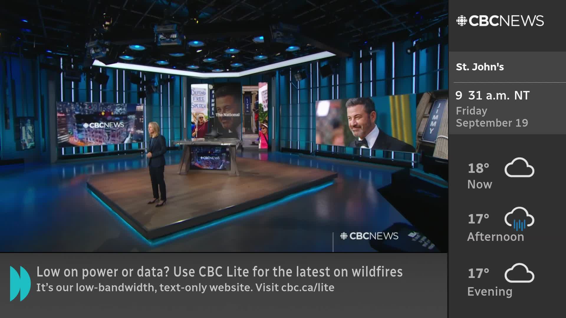 A woman in a dark suit stands on a raised platform in a CBC News studio, facing the camera. Behind her, large screens display images and the CBC News logo.
