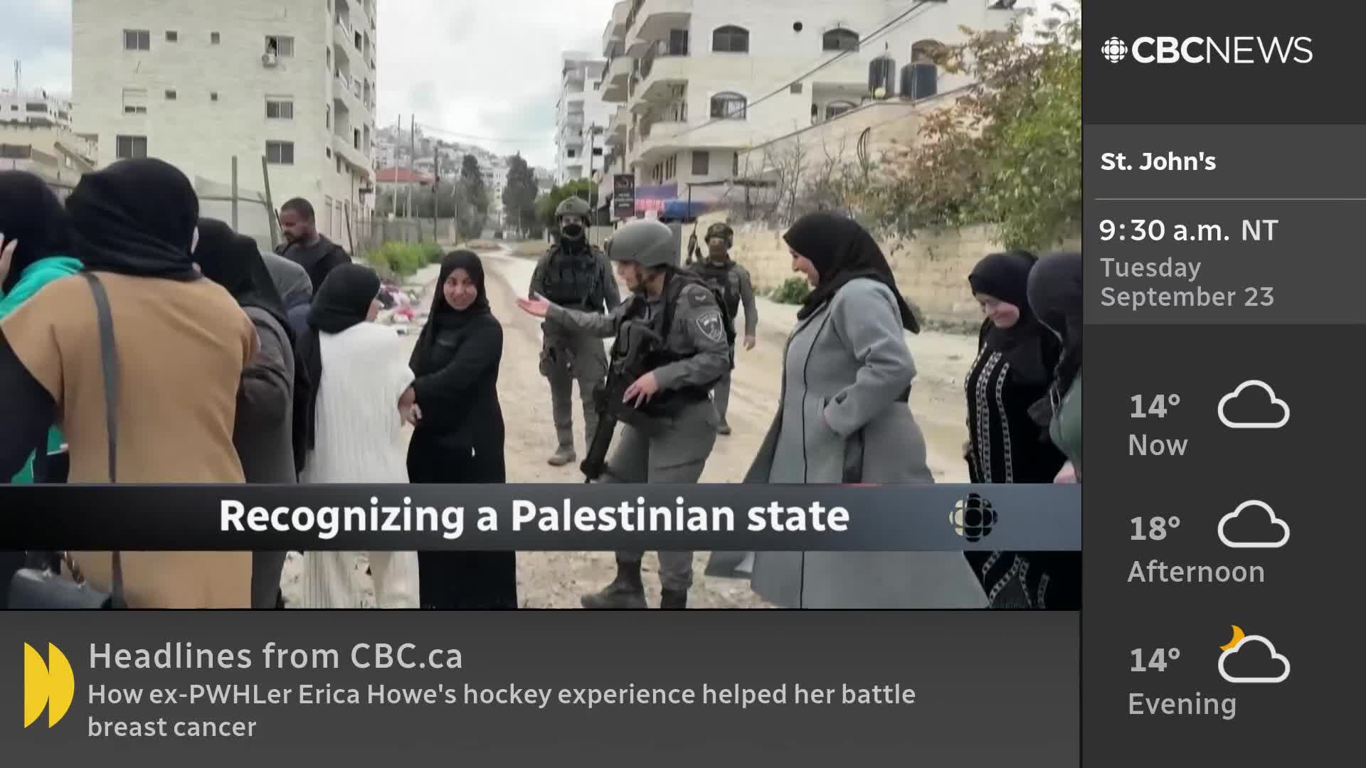 A group of women in headscarves and coats stand on a street, facing armed soldiers. One of the soldiers gestures with their hand, as if explaining something.

