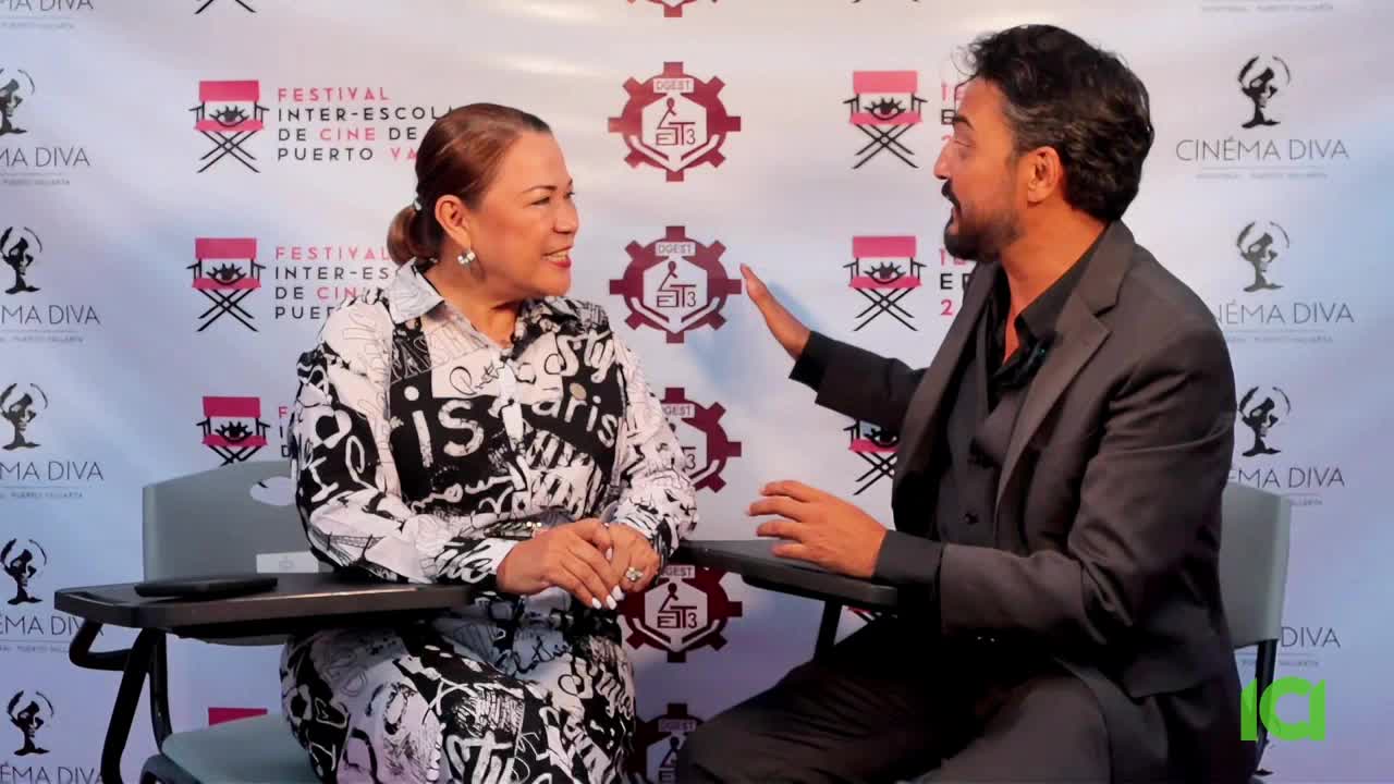 A woman in a patterned blouse listens intently while a man in a suit gestures with his right hand. They're seated at a table, likely for an interview at the film festival.
