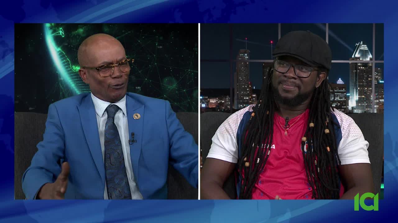 On CFHD-DT, a man in a blue suit gestures animatedly, speaking to someone off-screen. Across the screen, another man, wearing a cap and dreadlocks, listens intently.
