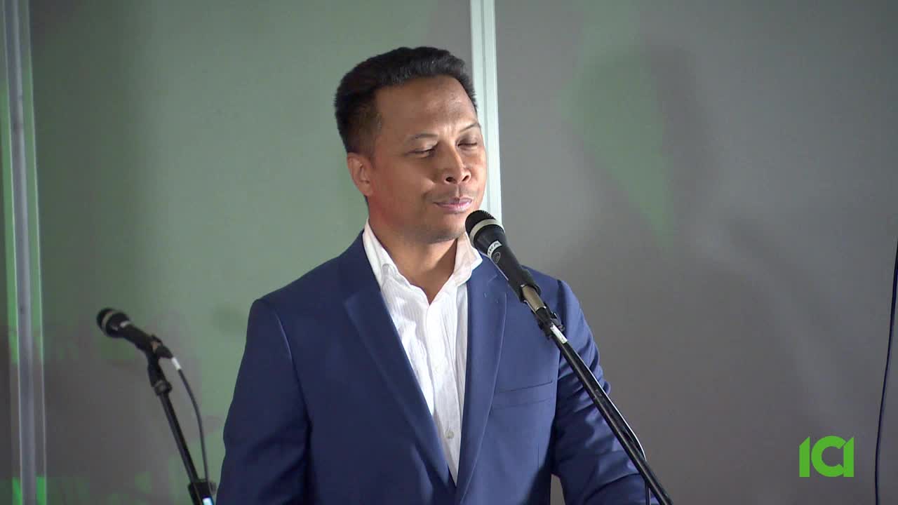 A man in a blue suit stands at a microphone, speaking. The logo for ICI Canada is visible in the corner.
