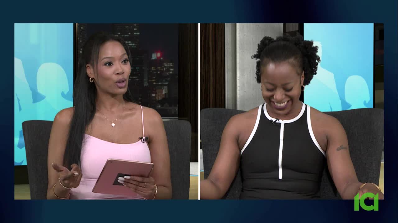 The woman in pink gestures with her hands while speaking, holding a tablet. Across from her, the other woman laughs, her face lit up with a smile.
