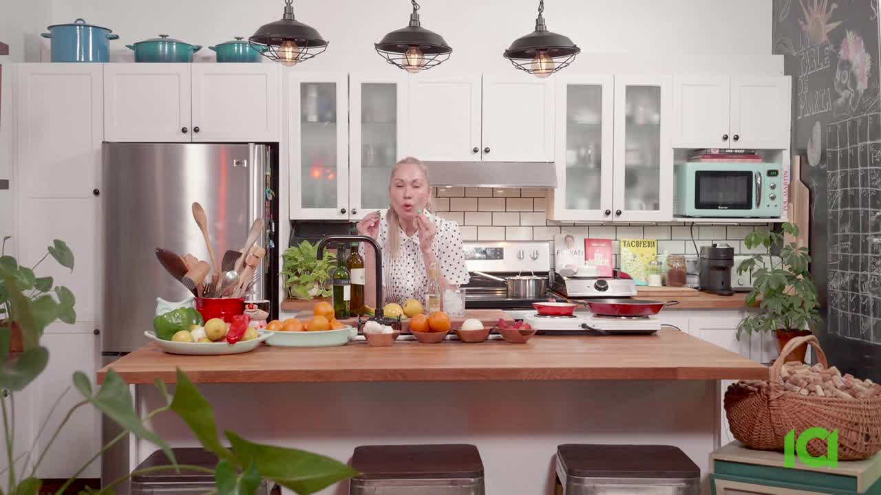 A woman in a polka-dot shirt gestures with her fingers, likely describing the food on the counter. The kitchen is brightly lit, with cooking equipment and ingredients neatly arranged for a CFHD-DT broadcast.

