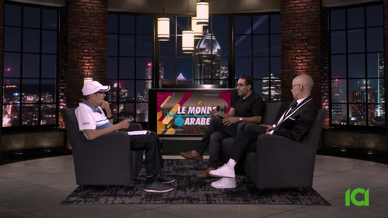 Three men are seated in armchairs, engaged in a discussion on a CFHD-DT set, with a cityscape visible through the windows behind them. The show's title, "Le Monde Arabe," is displayed on the screen behind the seated individuals.
