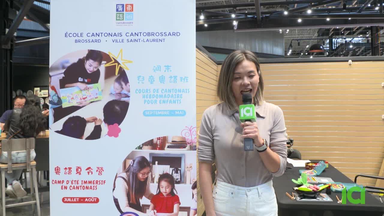 A woman with a microphone, likely a reporter for CFHD-DT in Canada, is speaking in front of a banner advertising Cantonese language classes for children. Behind her, a table holds some green toys and a few other items.
