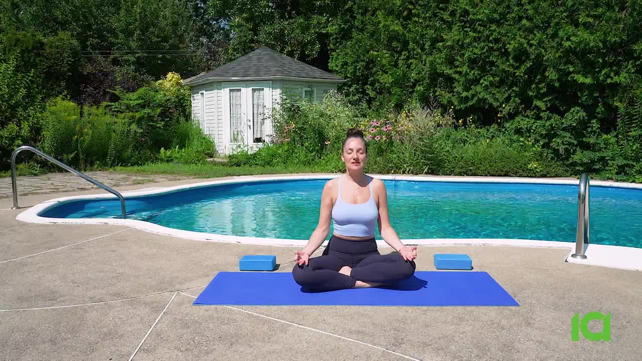A woman sits cross-legged on a blue mat, eyes closed, next to a pool on a sunny day. The CFHD-DT logo is visible in the corner.
