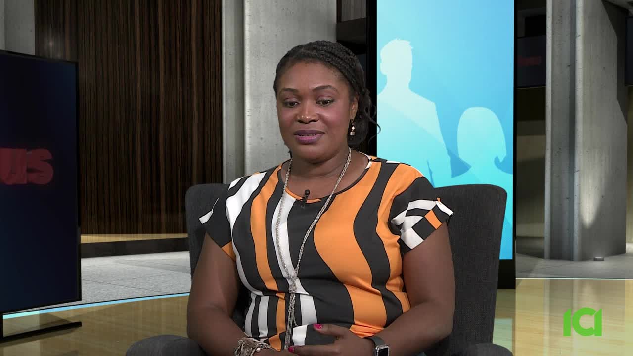 A woman in a patterned orange and black top sits in a chair, speaking. The CFHD-DT logo is visible in the corner and a screen with the word "NEWS" is behind her.
