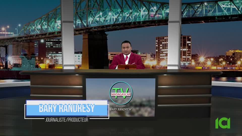 A man in a maroon jacket sits behind a desk with a screen displaying "TV Madagascar." Behind him, a cityscape with a bridge and buildings glows in the background.
A man in a maroon jacket sits behind a desk with a screen displaying "TV Madagascar." Behind him, a cityscape with a bridge and buildings glows in the background.