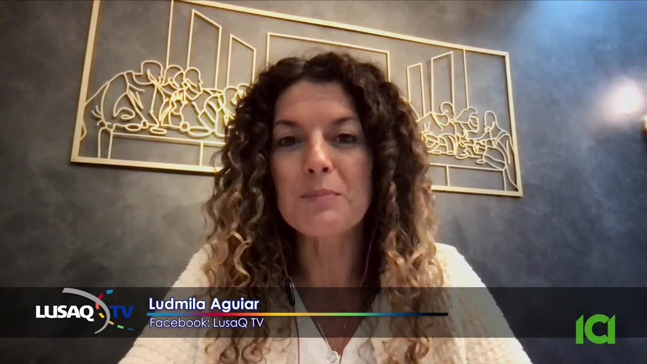 Ludmila Aguiar from LusaQ TV is speaking directly to the camera, her curly hair framing her face. Behind her, a golden wall hanging depicts a stylized scene.
Ludmila Aguiar from LusaQ TV is speaking directly to the camera, her curly hair framing her face. Behind her, a golden wall hanging depicts a stylized scene.