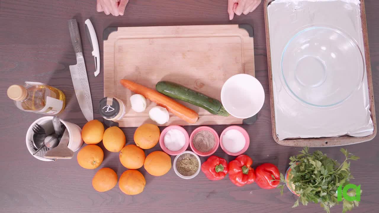 A collection of ingredients, including oranges, peppers, and zucchini, is laid out on a dark surface. A cutting board and a baking sheet with a glass bowl sit nearby, ready for preparation.
A collection of ingredients, including oranges, peppers, and zucchini, is laid out on a dark surface. A cutting board and a baking sheet with a glass bowl sit nearby, ready for preparation.
