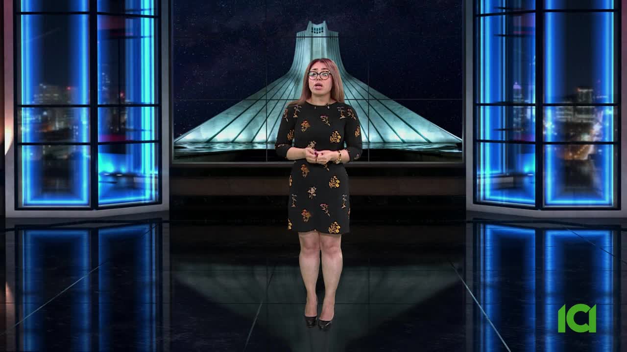 The woman in the floral dress stands centered, speaking in front of a backdrop featuring a large structure. Behind her, the set's glowing blue window frames reflect the studio lights.
The woman in the floral dress stands centered, speaking in front of a backdrop featuring a large structure. Behind her, the set's glowing blue window frames reflect the studio lights.