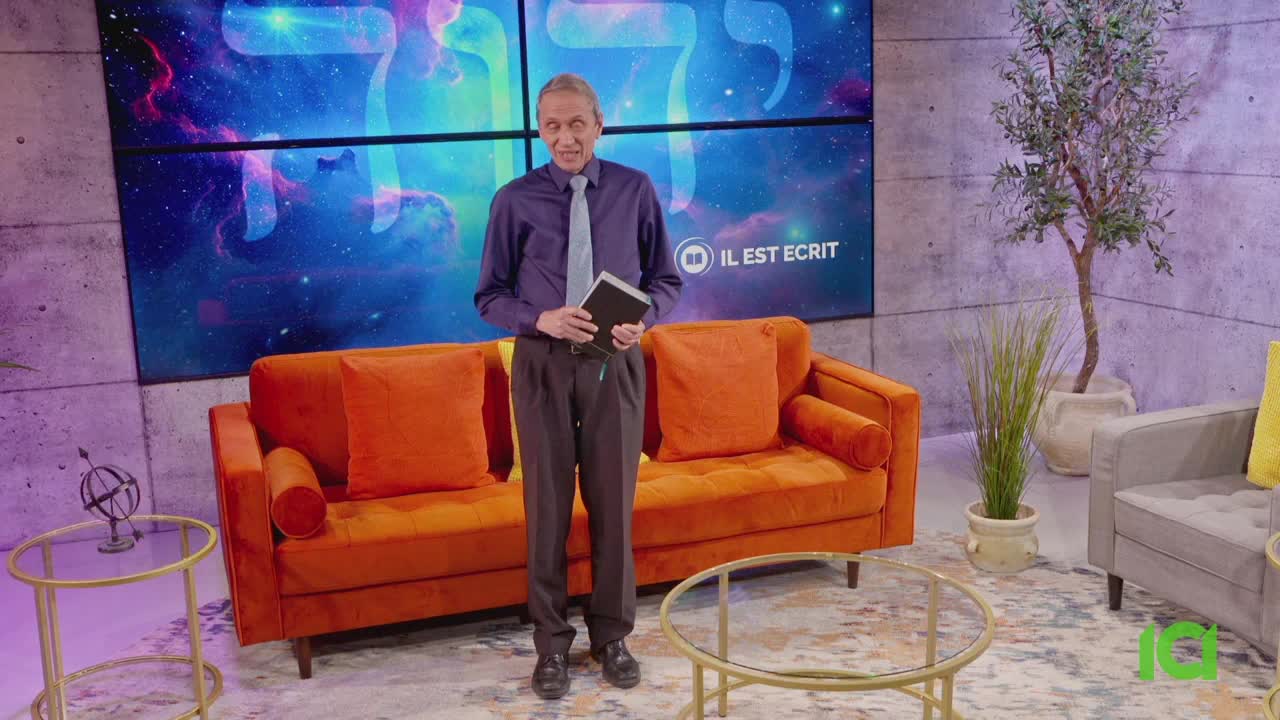 A man in a purple shirt and tie stands in front of a bright orange couch, holding a book. Behind him, the CFHD-DT logo for "Il Est Écrit" is displayed on a screen with a celestial background.
