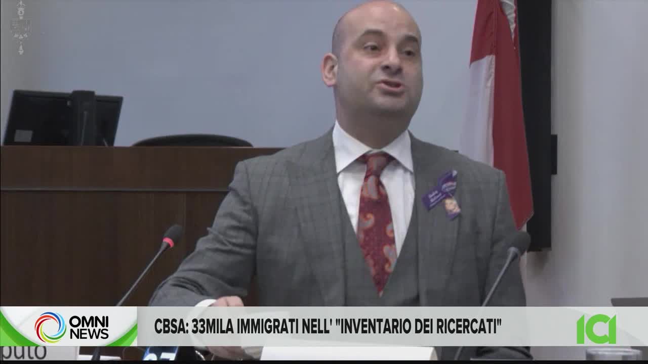 A man in a gray suit and patterned tie speaks at a podium, his mouth moving as he addresses the room. The CFHD-DT news logo, OMNI News, is visible at the bottom of the screen, with Italian text about immigration.
