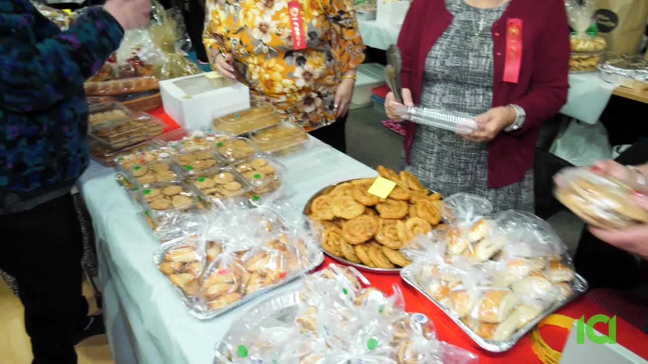 Tables overflow with baked goods, from cookies in plastic containers to golden pastries. People are gathered, reaching for treats at what looks like a community event.
