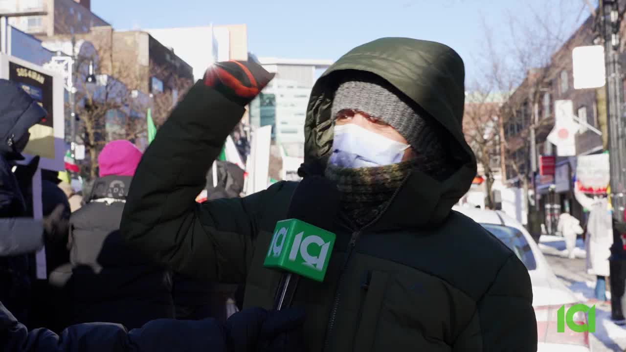 A reporter from 10 ICI is interviewing someone in a thick winter coat. The crowd behind them holds flags and signs, suggesting a protest is underway in a Canadian city.