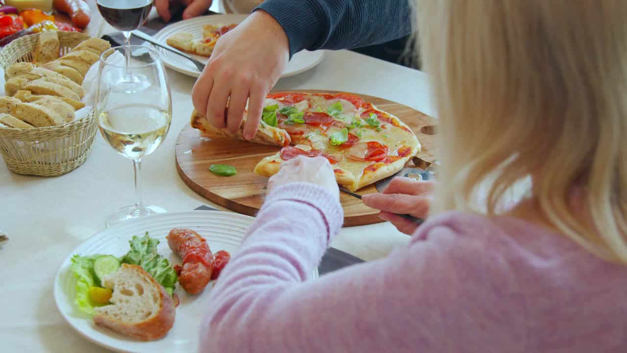A hand reaches for a slice of pizza, its crust golden brown. Another hand holds a knife, ready to cut into the cheesy pie.