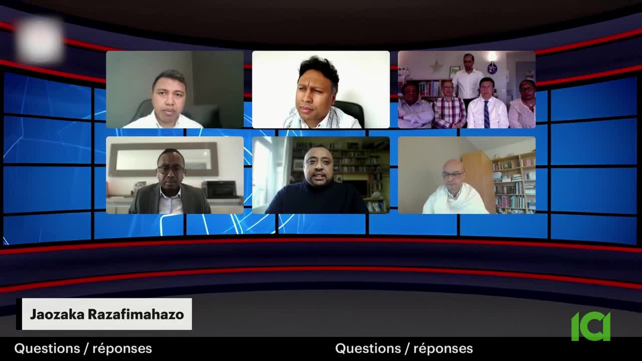 Six men appear on screen in separate video feeds, arranged in two rows of three. The bottom row features a man in a dark turtleneck, another in a suit, and a third in a white scarf. The top row shows three more men, one in a white shirt, another in a plaid shirt, and a third in a light pink shirt.