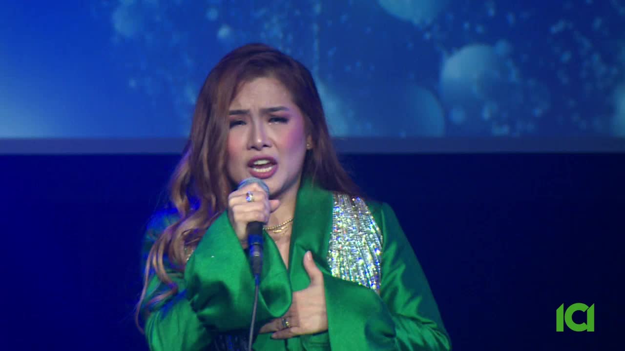 A singer in a vibrant green jacket belts into a microphone, her hand resting on her chest. The ICI logo appears in the lower right corner.