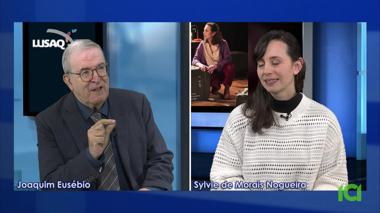 Joaquim Eusébio gestures emphatically while speaking, his tie slightly askew. Sylvie de Morais Nogueira sits across from him, a faint smile on her face, her white sweater catching the light.