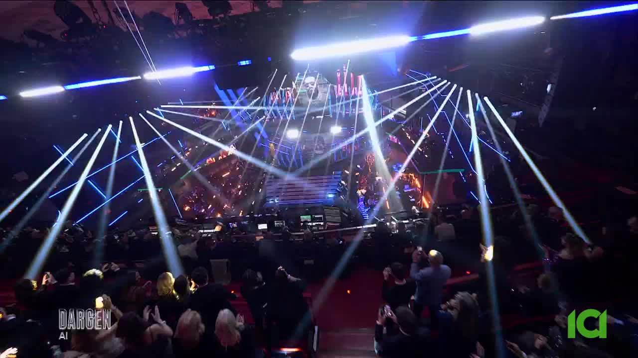 Bright white and blue lights slash across the stage, illuminating a massive crowd. The ICI logo glows green in the corner, a familiar sight for viewers across Canada.