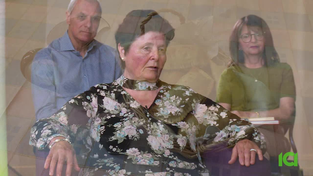 A woman in a floral blouse speaks, her gaze directed slightly off-camera. Behind her, a man in a blue button-down shirt and a woman in a green top are visible, their forms slightly blurred. The CFHD-DT logo appears in the lower right corner. A woman in a floral blouse speaks, her gaze directed slightly off-camera. Behind her, a man in a blue button-down shirt and a woman in a green top are visible, their forms slightly blurred. The CFHD-DT logo appears in the lower right corner.