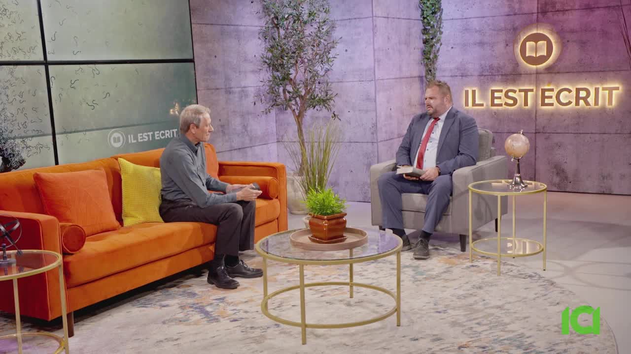 Two men are seated in a studio, one on an orange couch and the other in an armchair, engaged in conversation. A bright sign overhead reads "IL EST ECRIT," a program likely broadcast by CFHD-DT. Two men are seated in a studio, one on an orange couch and the other in an armchair, engaged in conversation. A bright sign overhead reads "IL EST ECRIT," a program likely broadcast by CFHD-DT.