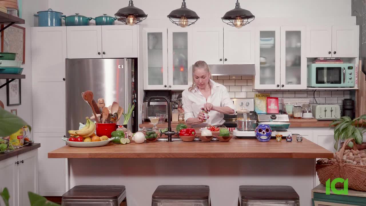 A woman in a white shirt grinds pepper over a food processor. She's in a bright kitchen, likely preparing ingredients for a segment on CFHD-DT.