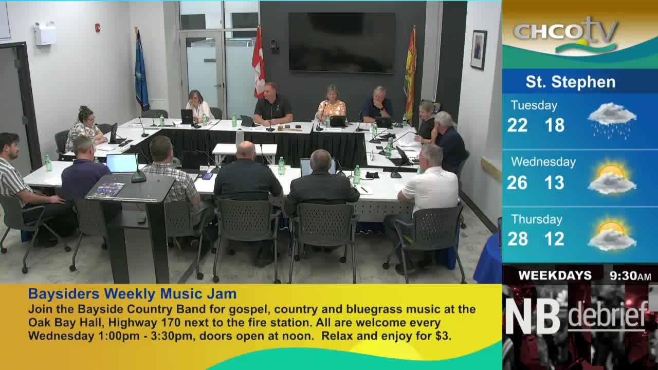 A meeting is underway, with people seated around a large table, some with laptops open. The CHCO-TV weather forecast for St. Stephen is displayed on the side.

