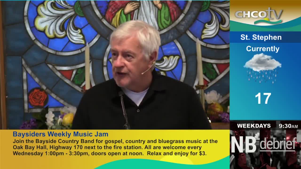 A man with white hair speaks into a microphone, likely on CHCO-TV, with a stained-glass window behind him. The screen shows the weather in St. Stephen, Canada, and details about a weekly music jam.

